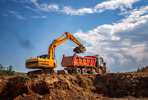 Transportation of a dirty excavator on a truck trailer after its work. Motion speed and blur effect on city highway, during sunset sky