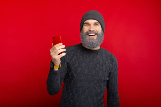 istock Young smiling man with beard holding red smartphone and looking confident at the camera 1189381630