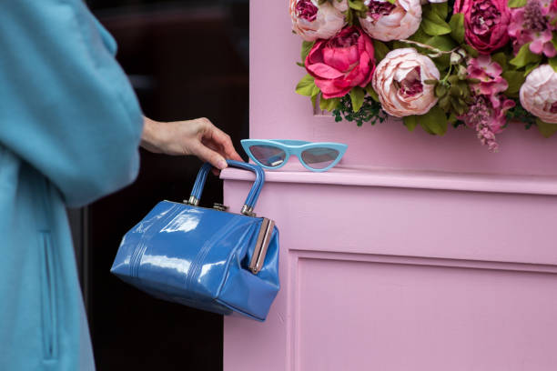 Blue sunglasses and a purse against a pink wall