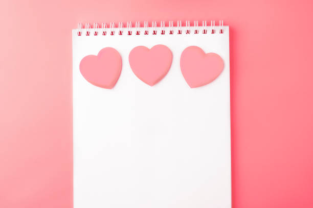 istock Valentines day background. Open blank notebook and pink hearts on a pink peach background. Writing romantic letters. Top view. Copy space 1189383174
