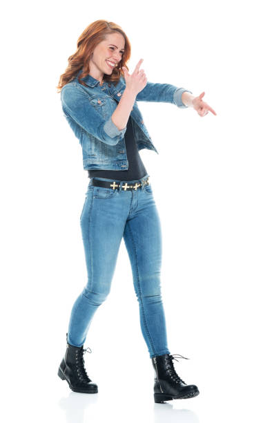 full length / side view / profile view / one person of 20-29 years old adult beautiful redhead / long hair caucasian female / young women walking wearing double denim / jeans / pants / denim jacket / boot / rolled-up sleeves / jacket / warm clothing - one young woman only only young women one woman only 20 25 years imagens e fotografias de stock