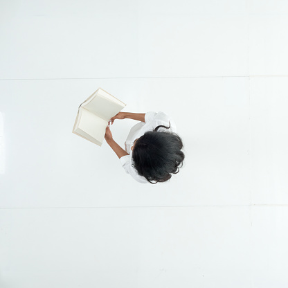 One person / full length / directly above view / aerial view of 20-29 years old adult beautiful black hair / long hair latin american and hispanic ethnicity female / young women student / university student standing in front of white background wearing button down shirt / shirt who is learning / studying / cool attitude and holding book / textbook with copy space