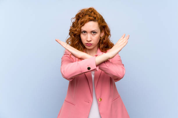 istock Redhead woman in suit over isolated blue wall making NO gesture 1189403747