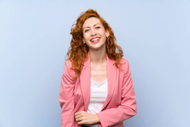 istock Redhead woman in suit over isolated blue wall smiling 1189405609