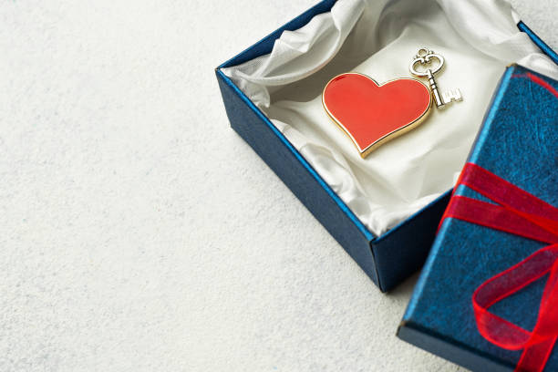 istock Open blue box with a gift and a red ribbon on a light background with place for text with red heart and key 1189419695