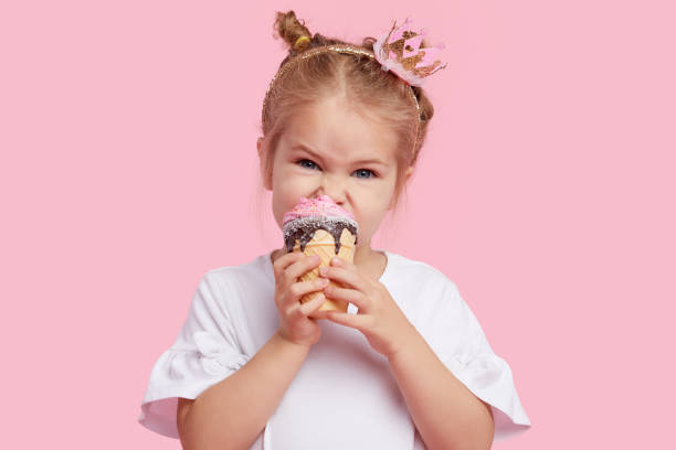 istock Cute child girl with pleasure eats tasty ice-cream on a pink studio background. Licks with closed eyes. The concept of baby food and a happy childhood 1189419829