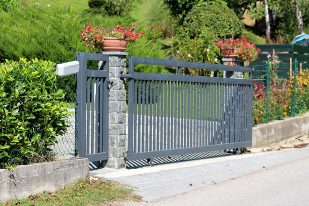 istock Thick strong metal sliding front yard driveway entrance doors mounted on stone column surrounded with wire fence and garden vegetation 1189421597