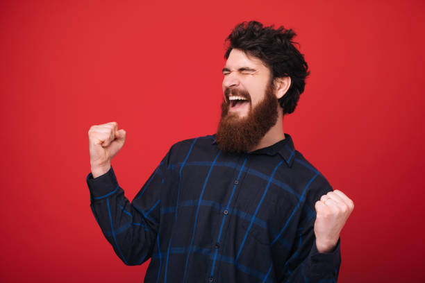 istock Bearded man closing eyes and celebrating with rised hands over red background 1189422632