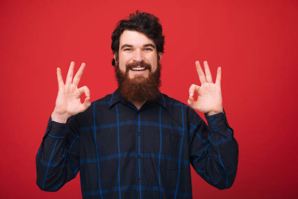 istock OK ! Smiling guy with beard showing ok sign with both hands over red isolated background 1189422988