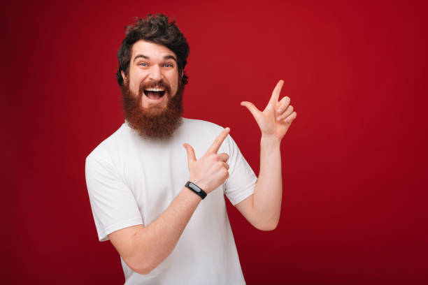 istock Excited man with beard pointing up  at copyspace while looking at camera over red background 1189423371