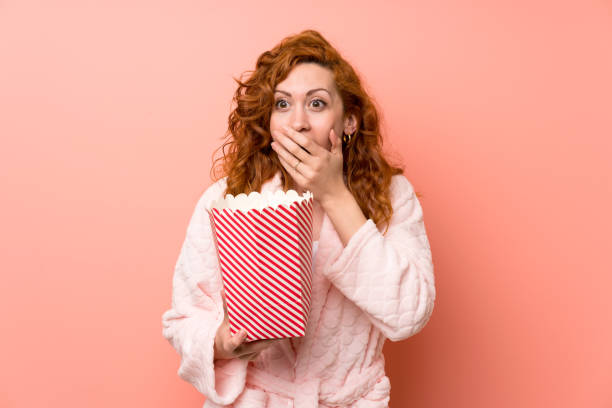 istock Redhead woman in dressing gown eating popcorns 1189432368
