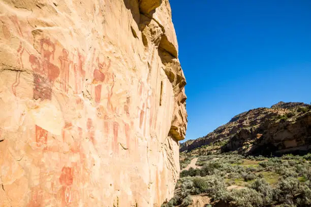 Photo of Pictographs of many figures in Central Utah on orange and red sandstone.