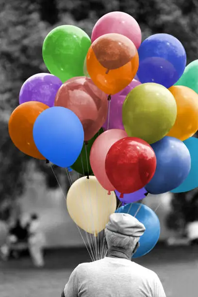 A black and white image of a man holding balloons with the balloon's colors added afterwards