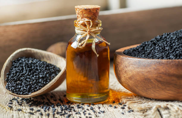 glass bottle of black cumin seeds essential oil , Nigella Sativa in spoon on wooden background stock photo