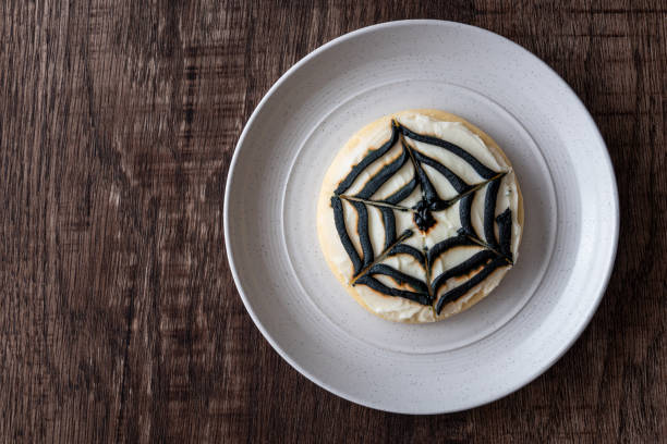 Halloween treat Creepy Halloween treat, spider web decorated sugar cookie on a white plate, dark wood table round sugar cookie stock pictures, royalty-free photos & images