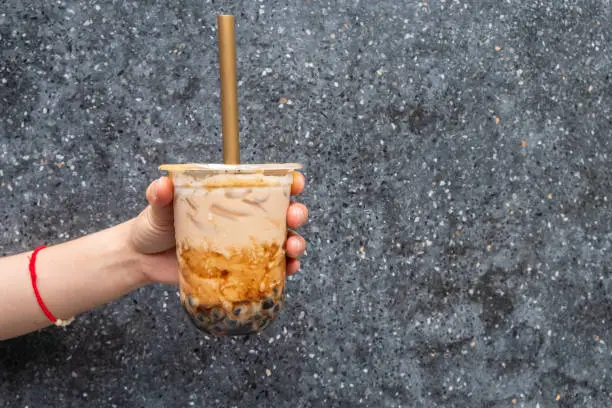 Photo of Cropped shot of someone hand holding a cup of iced Bubble milk tea with big straw.