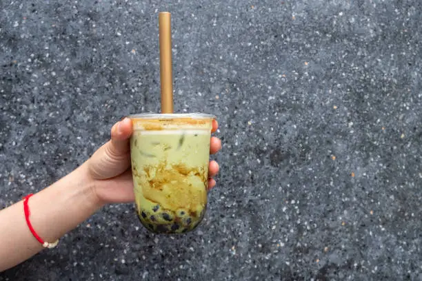 Photo of Cropped shot of someone hand holding a cup of iced Bubble matcha green tea with big straw.