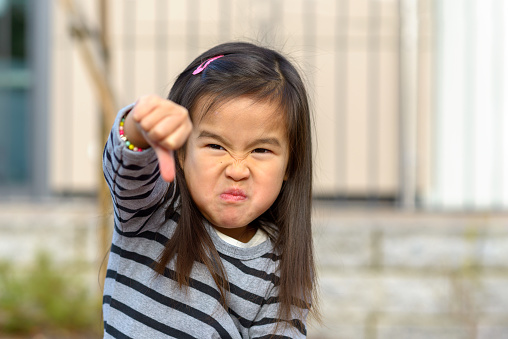 Angry frustrated little girl throwing a temper tantrum punching her fist at the camera with a furious vengeful expression outdoors