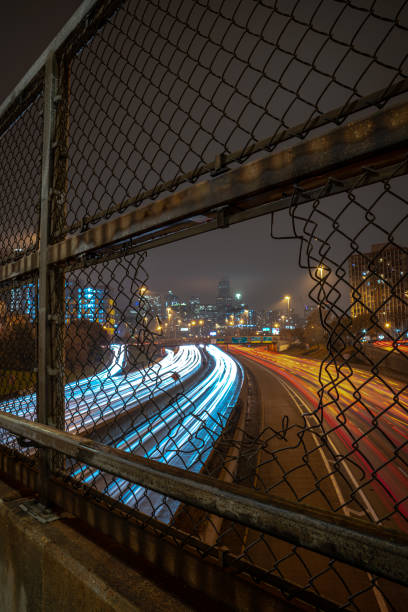 istock White and red light trails coming and going to downtown Chicago on a cloudy misty night viewed through an opening in a chain link fence guard rail on an overpass above highway or expressway at night. 1189478601