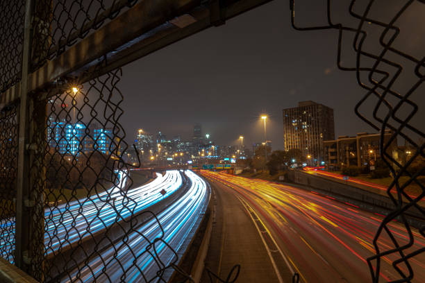 istock White and red light trails coming and going to downtown Chicago on a cloudy misty night viewed through an opening in a chain link fence guard rail on an overpass above highway or expressway at night. 1189478618