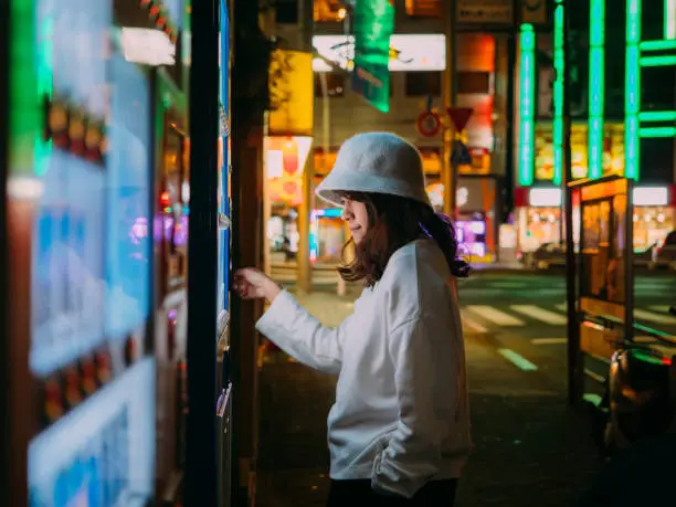 Asian woman paying with smartphone to vending machine.