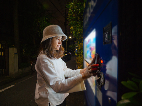Young asian woman paying with her smartphone to vending machine for drink in Japan.