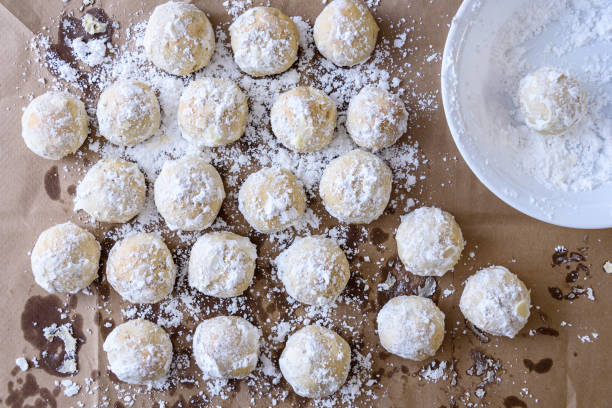 Holiday Baking Finished holiday batch of Russian Tea Cake cookies covered in powered sugar cooling on brown paper, white bowl powdered sugar stock pictures, royalty-free photos & images