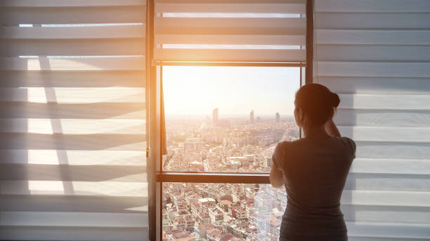 woman is opening blinds, looking at window with panoramic city view - sunny apartment window sky imagens e fotografias de stock