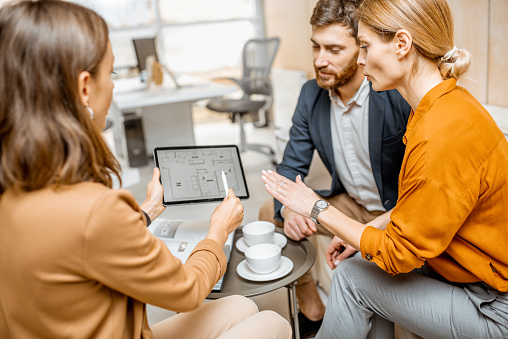 Young and lovely couple choosing a new house to buy, looking on the projects with a sales manager in the office of real estate agency