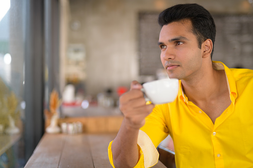 Portrait of young handsome Indian man sitting at the coffee shop