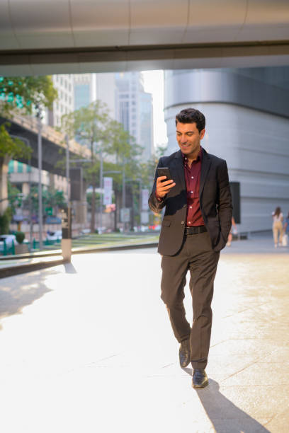 istock Young happy Hispanic businessman using phone outside the office building 1189491262