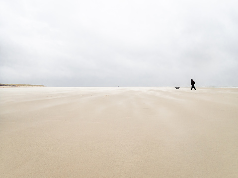 A man and his dog walking on the fine sandy  beaches of the Langeog island in Germany in Autumn