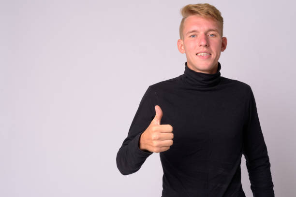 Portrait of happy young blonde man giving thumbs up Studio shot of young man with blond hair against white background high collar stock pictures, royalty-free photos & images