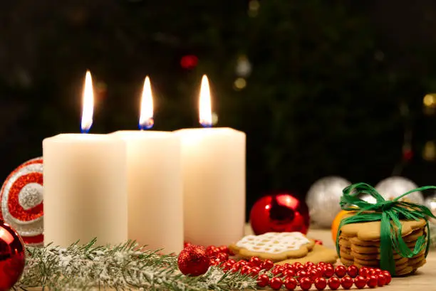 three burning candles with Christmas decoration from pine cones around. photo