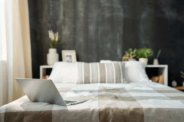 istock Open laptop on neatly made bed with linen checkered plaid and pillows 1189506805