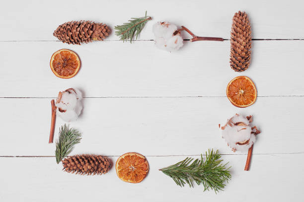 istock Craft envelope on white wooden desk. Decorative frame from pine cones, orange slices, cotton and fir branches. 1189507038