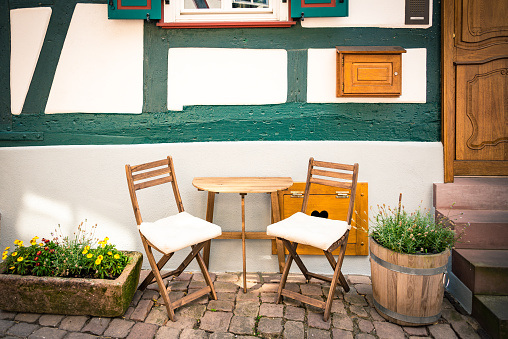 Cosy wooden table and chairs set in front of a typica german old style house.