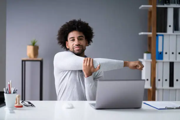 Young Businessman Stretching His Arms With Laptop On Desk