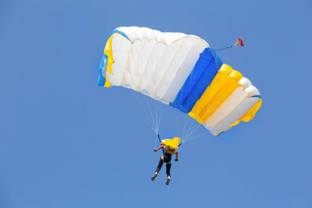 istock Skydiver under canopy of yellow with blue parachute in cloudless sky 1189513268