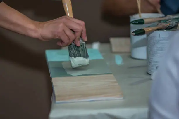 Teacher´s hand is showing how to work with the acrylic color and the brush applying color over a piece of wood. Indoor picture. Spain