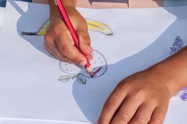 Drawing a strawberry on the drawing table. Child is concentrated drawing circle shapes on a piece of paper. Outdoor activity. Spain