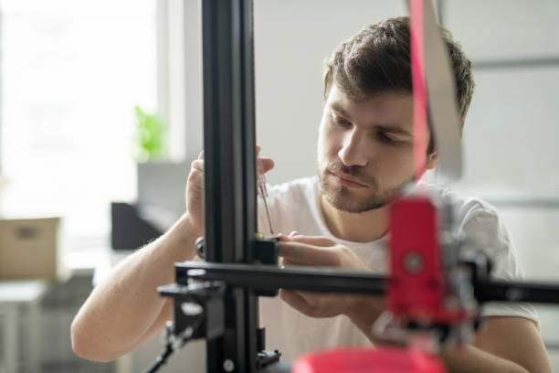 istock Young businessman standing in front of 3d printer while fixing some details 1189516574