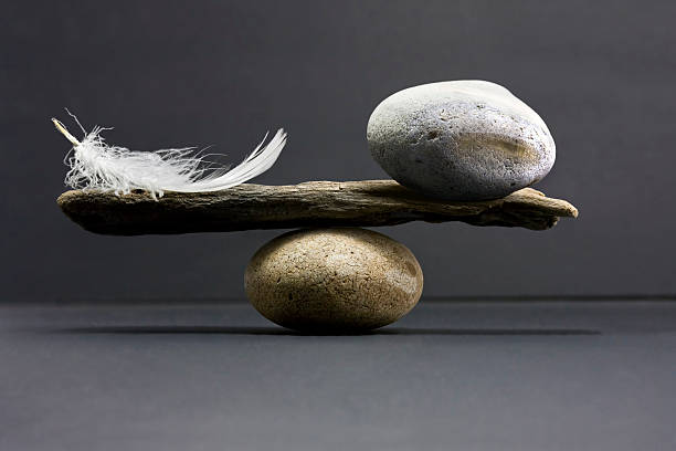 feather and stone balance A feather and a stone equally balanced, studio shot with dark lighting set up. lightweight stock pictures, royalty-free photos & images
