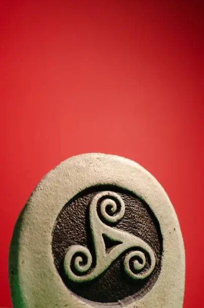 Decorative stone figure with the symbol of a celtic triskele or triskelion. Red background, empty space on the top