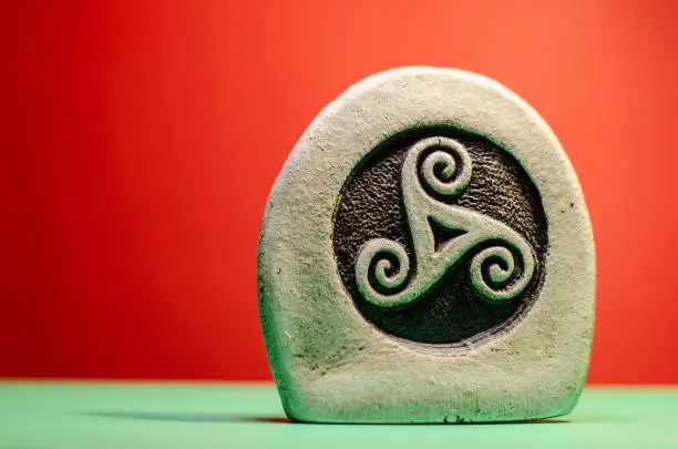 Decorative stone figure with the symbol of a celtic triskele on a green surface, red background