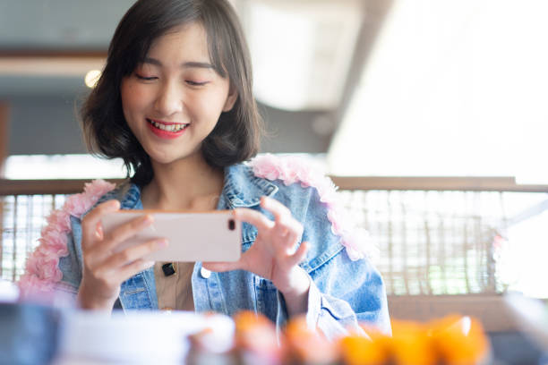 nahaufnahme junge süße asiatische japanische frau lächelnd, während mit dem smartphone, um foto von sushi auf gericht am restaurant-tisch zu nehmen und laden sie auf social-media-netzwerk für asiatische esskultur tradition konzept - essen zubereiten fotos stock-fotos und bilder