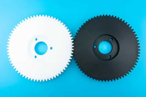 Connected black and white plastic gear with 68 sprockets on a blue background with copy space on the sides. Flat view from above.