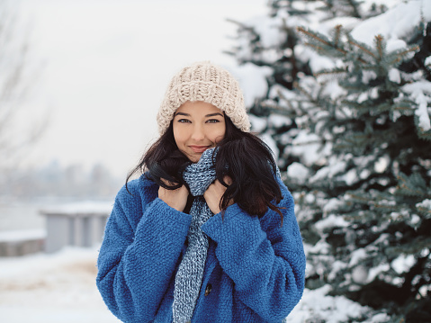 Beauty girl on the winter background. Close up portrait of young mixed race Caucasian Asian woman outdoors in a winter city park. Happy smiling woman in warm clothing looking to the camera