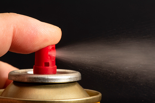 Closeup of the spray produced by a can valve in front of a black background