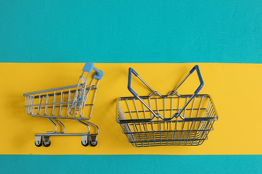 Minimalistic shopping concept. Shopping basket and trolley on blue-yellow background. Top view